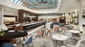 A spacious lobby with a high ceiling, a central bar area, seating arrangements, and a large glass dome structure. - Hilton Long Island/Huntington (Melville)
