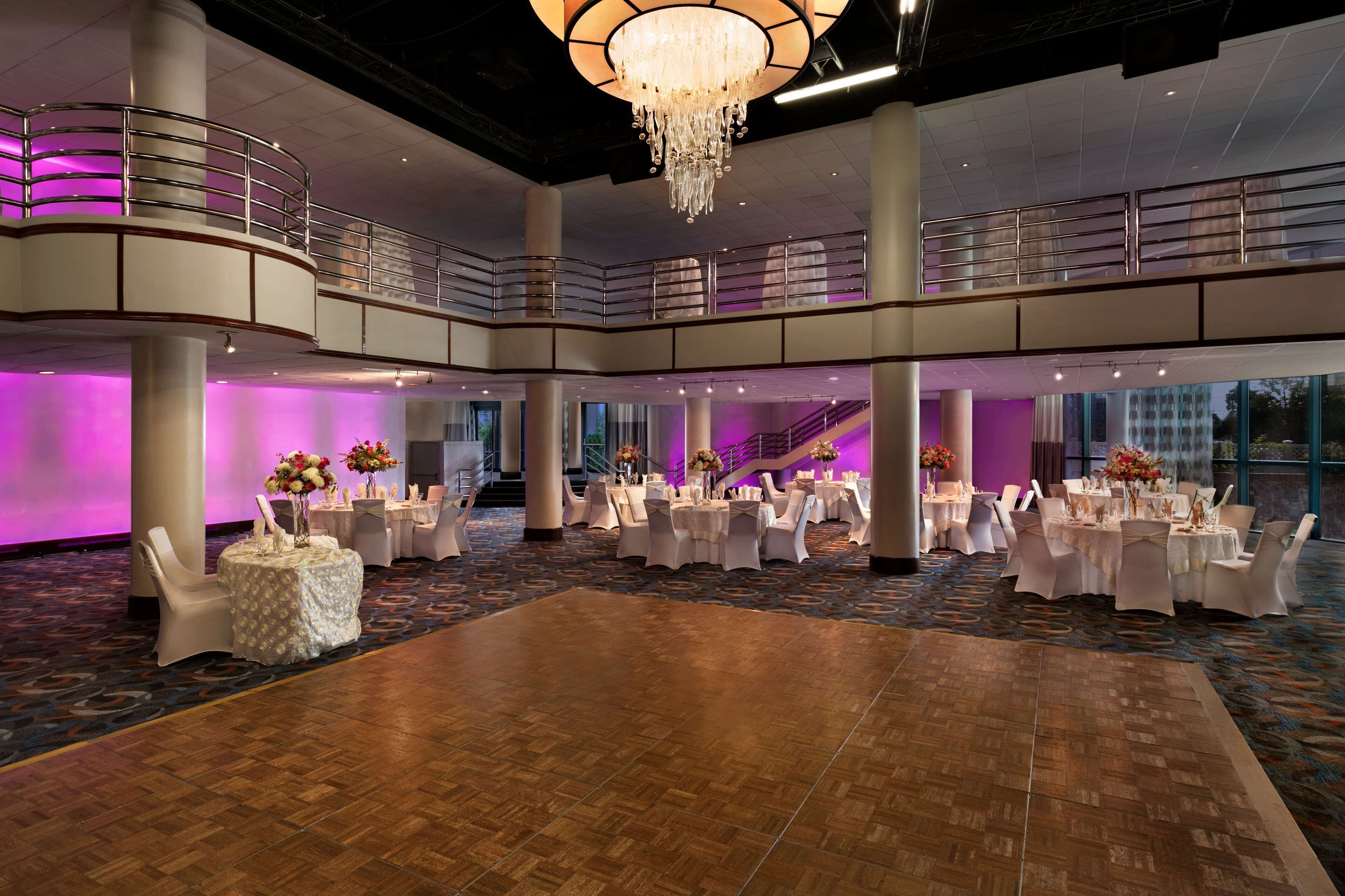 A spacious ballroom with multiple round tables, a central dance floor, and a balcony with a railing.