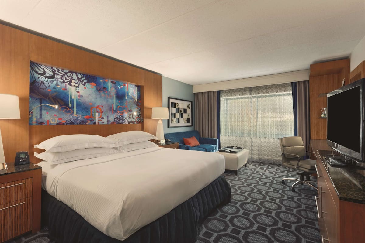 Habitación de hotel con una cama grande, un escritorio, una silla, un televisor y una ventana con cortinas.