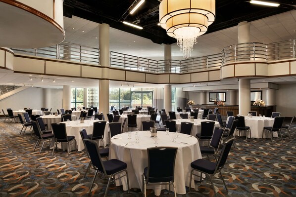 A spacious conference room with multiple round tables, chairs, and a chandelier. - Hilton Long Island/Huntington (Melville)