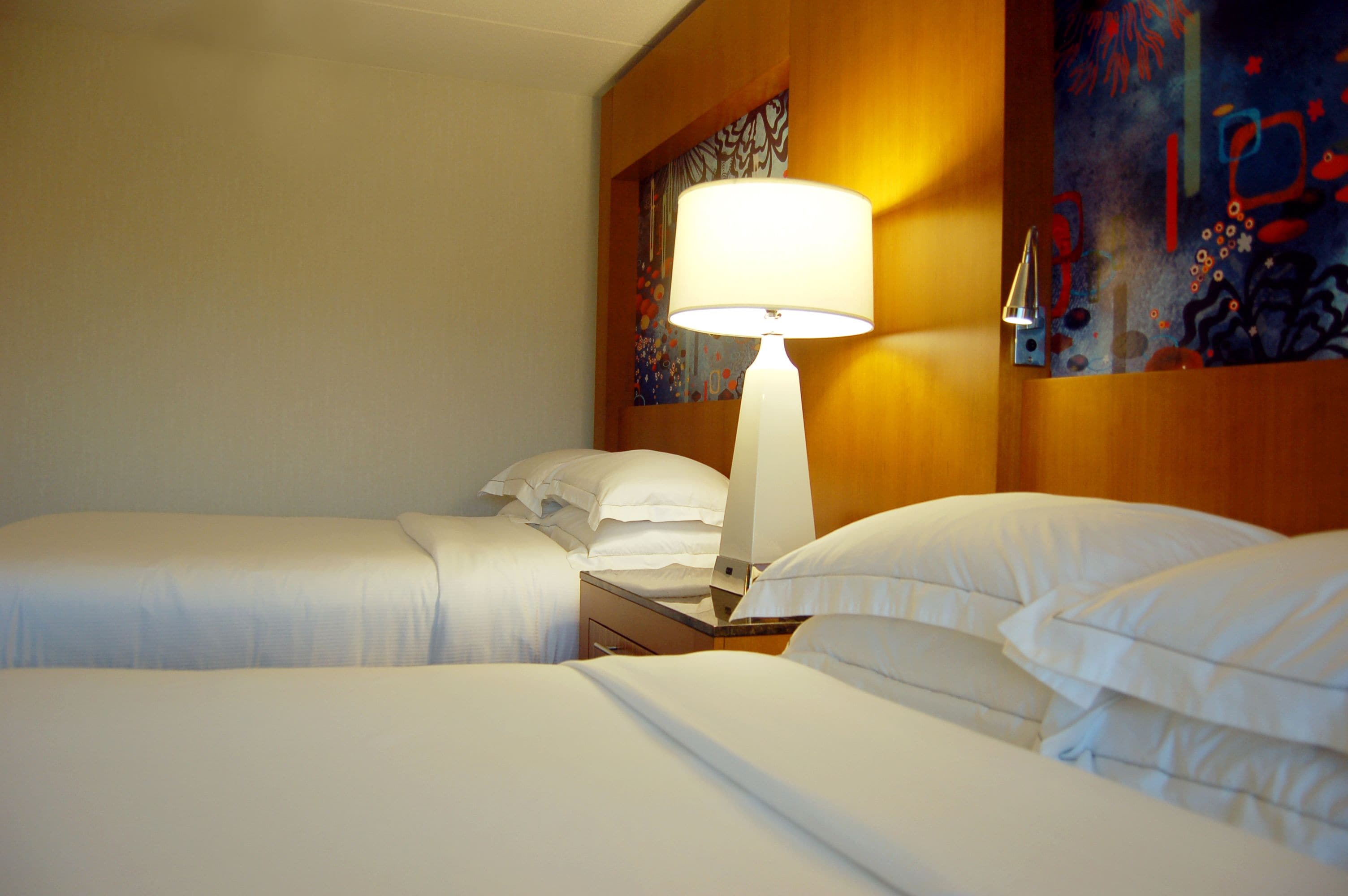 A hotel room with two beds, a nightstand with a lamp, and artwork on the walls.