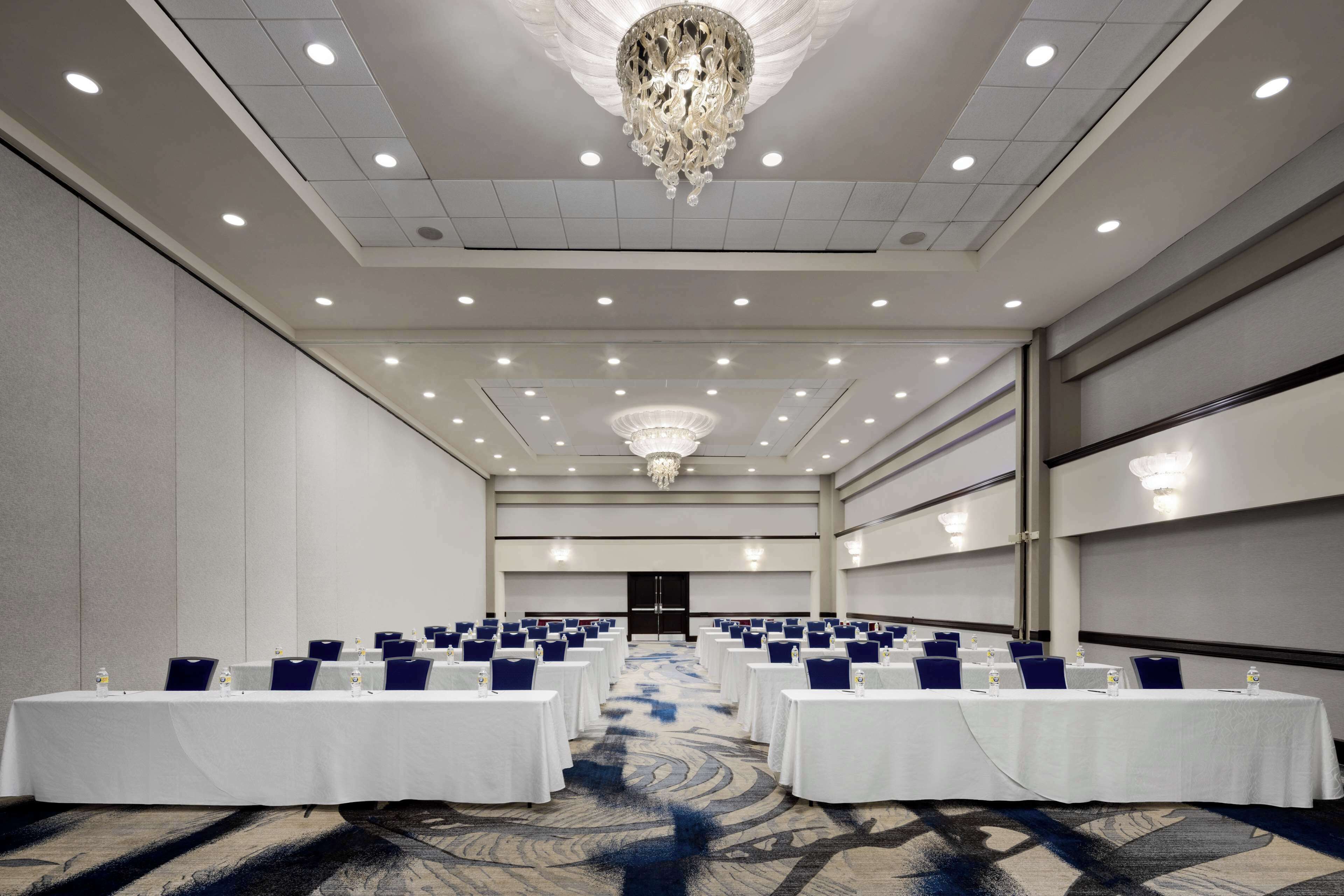 A conference room with rows of tables, a chandelier, and a carpeted floor.