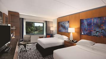 A hotel room with two beds, a desk, a chair, a TV, and a painting on the wall.