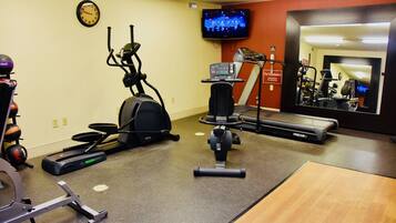Een sportschool met trainingsapparatuur, een klok en een televisie aan de muur.