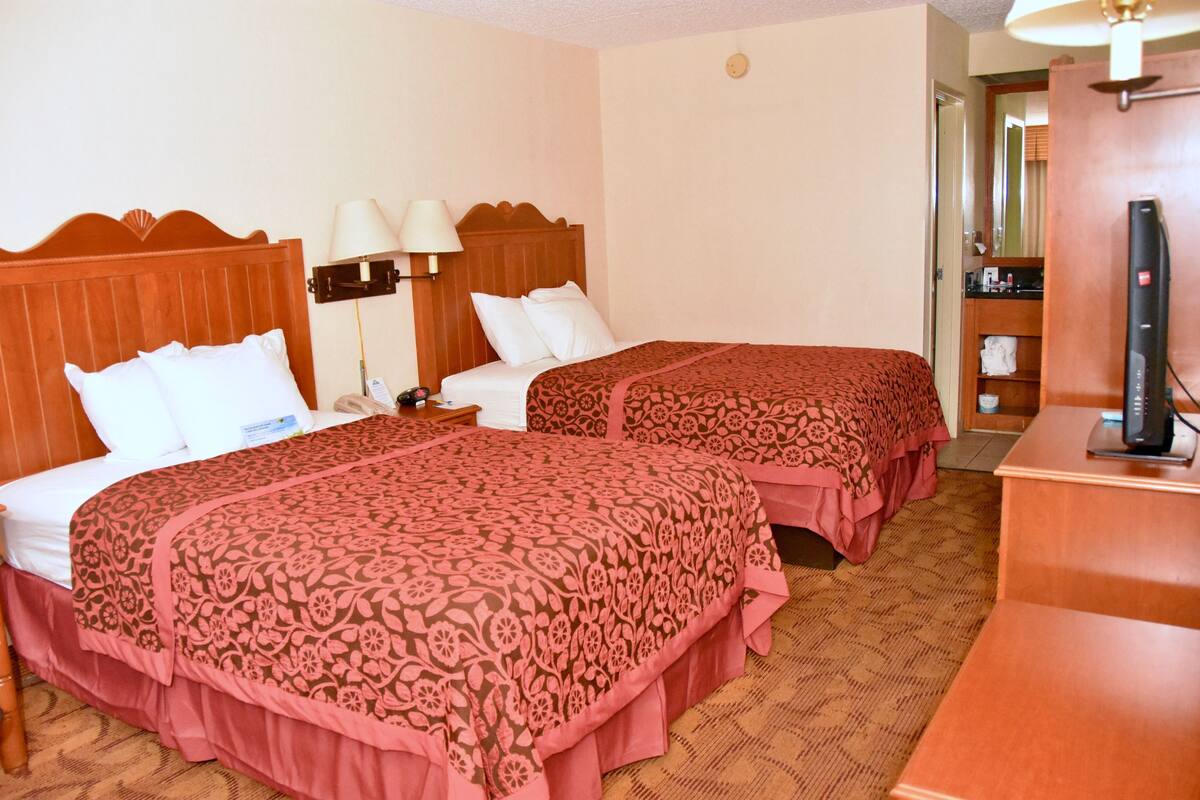 A hotel room with two beds, a desk, a TV, and a bathroom visible through an open door.