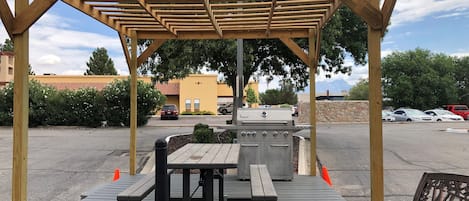 Un espace extérieur abrité comprenant un barbecue, des tables de pique-nique et des bancs.