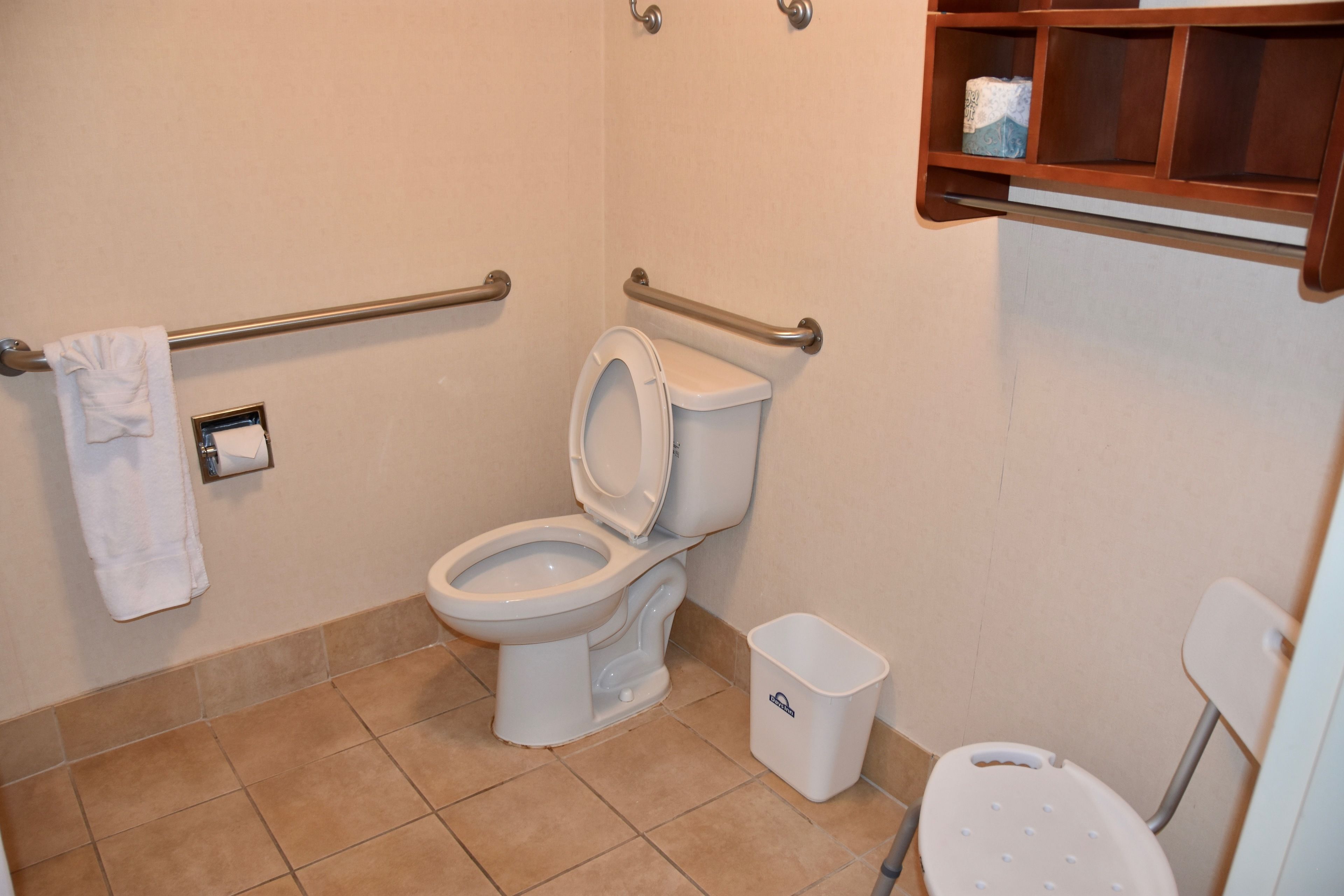 A bathroom with a toilet, a handrail, a trash bin, and a shelf with toiletries.