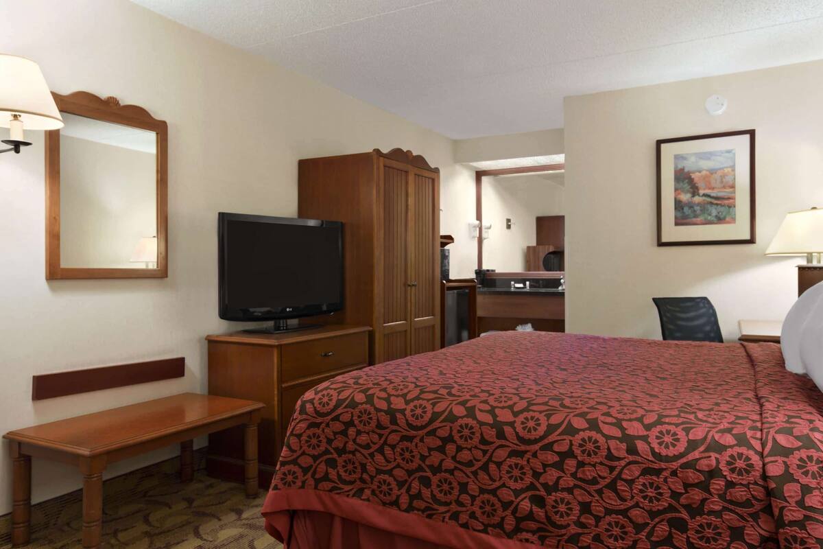 A hotel room with a bed, a television, a wooden wardrobe, a desk, and a chair.