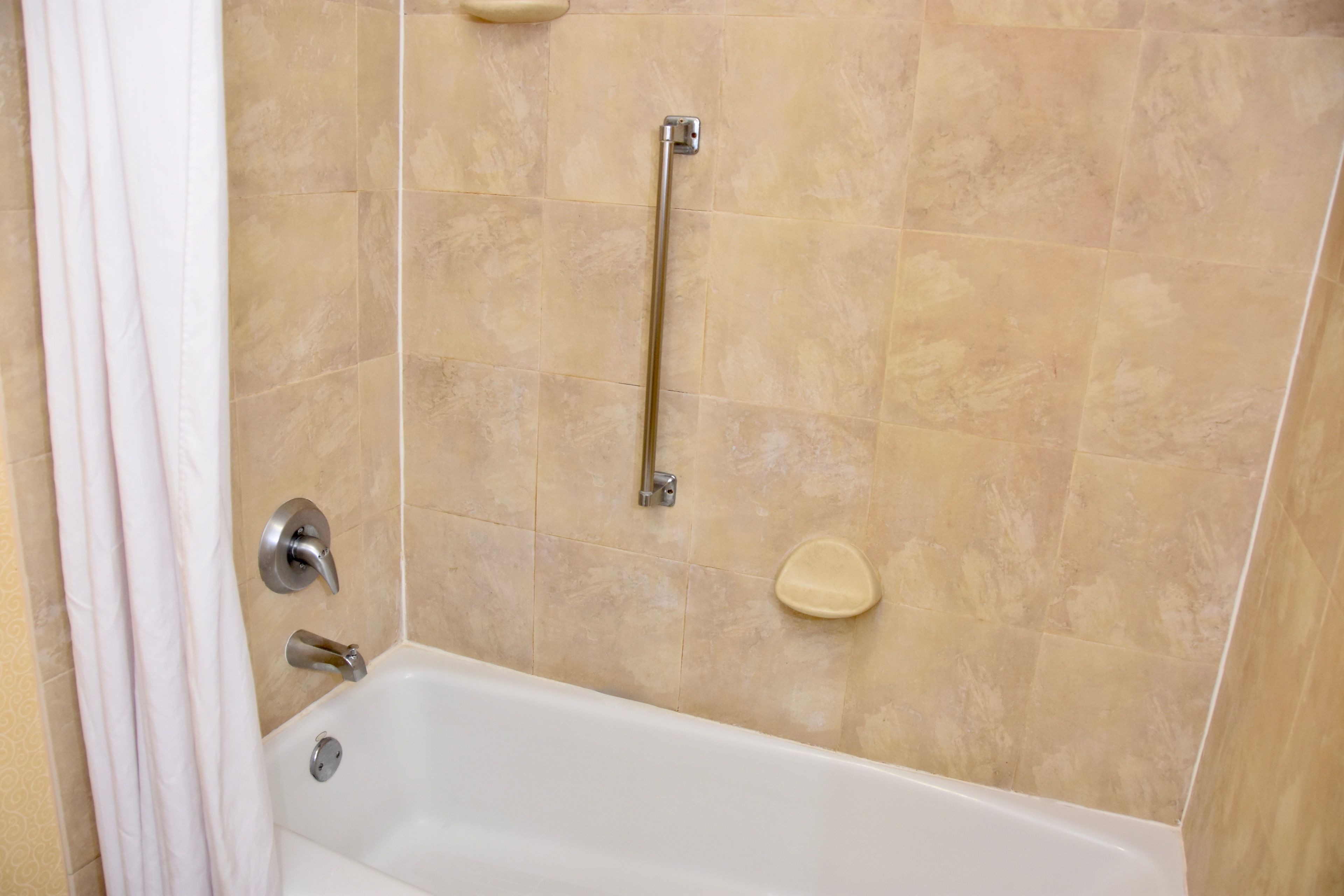 A bathroom with a bathtub, a handrail, and a shower curtain.
