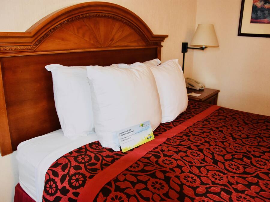 Una cama bien hecha con colcha de cuadros rojos y negros, un cabecero de madera y una mesita de noche con una lámpara y un teléfono.
