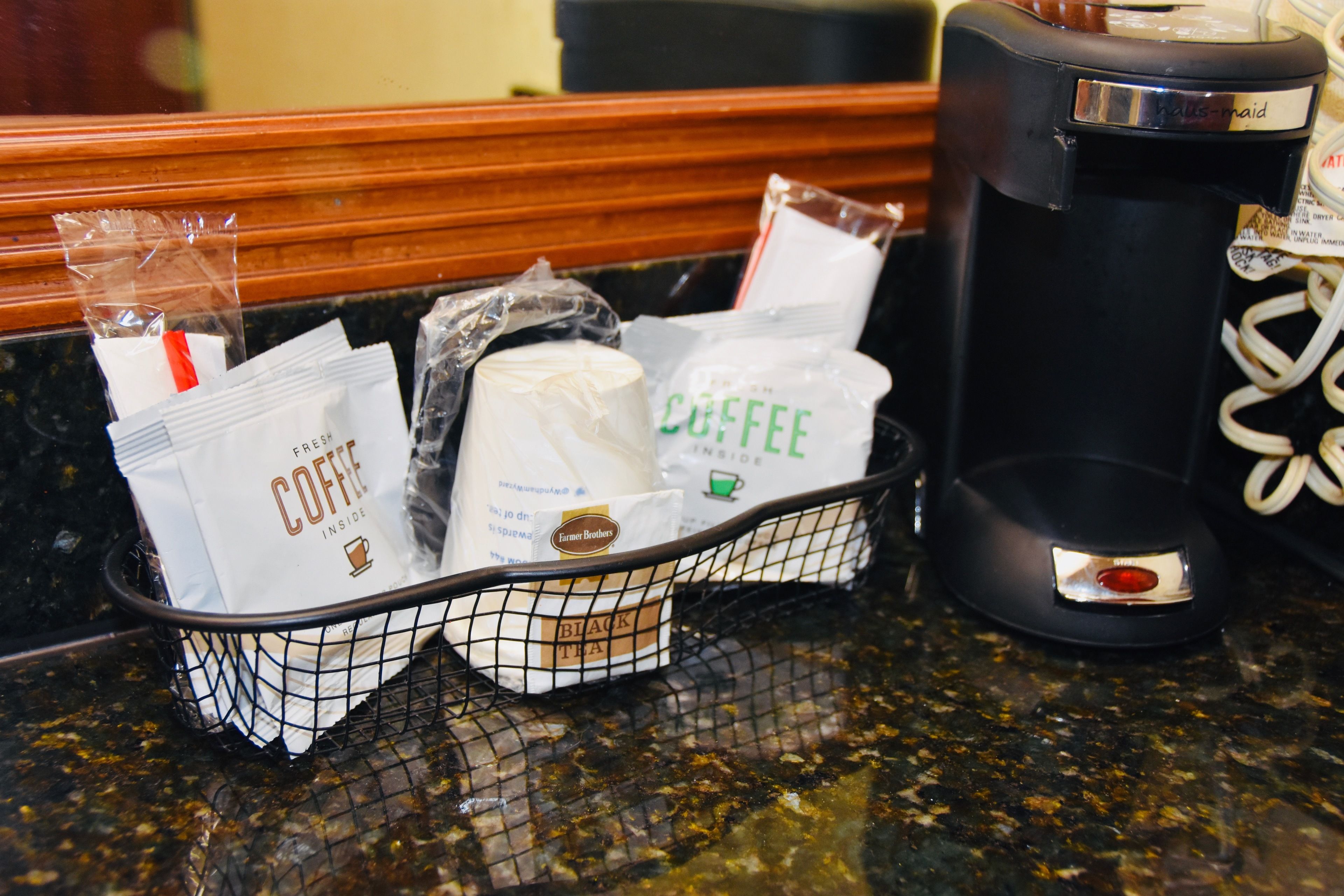 A coffee station with a basket containing coffee packets and a coffee maker.
