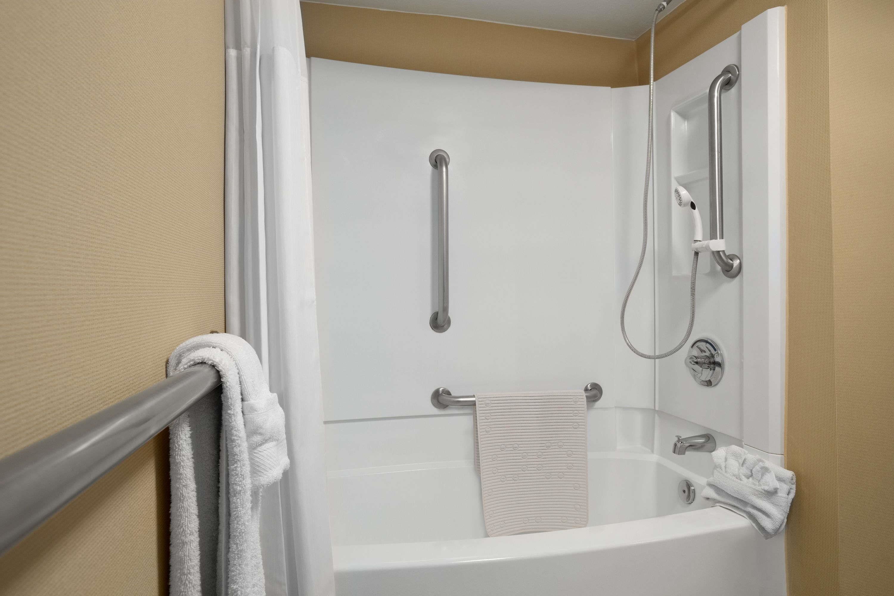 A corner shower with a glass partition, grab bars, and a handheld showerhead.