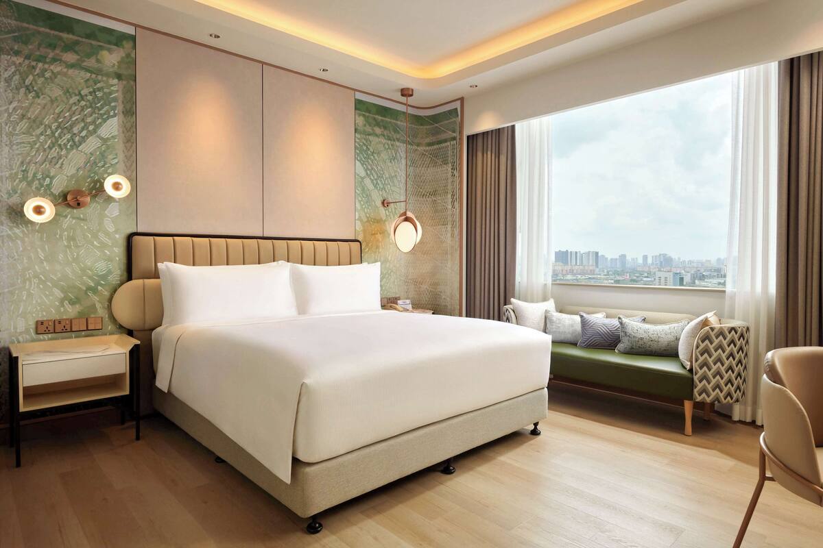 A modern hotel room with a large bed, a seating area, and a city view.