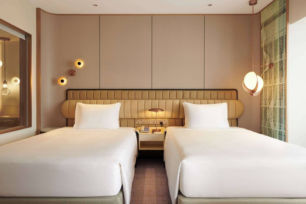 A hotel room with two beds, a nightstand, a lamp, and a mirror.