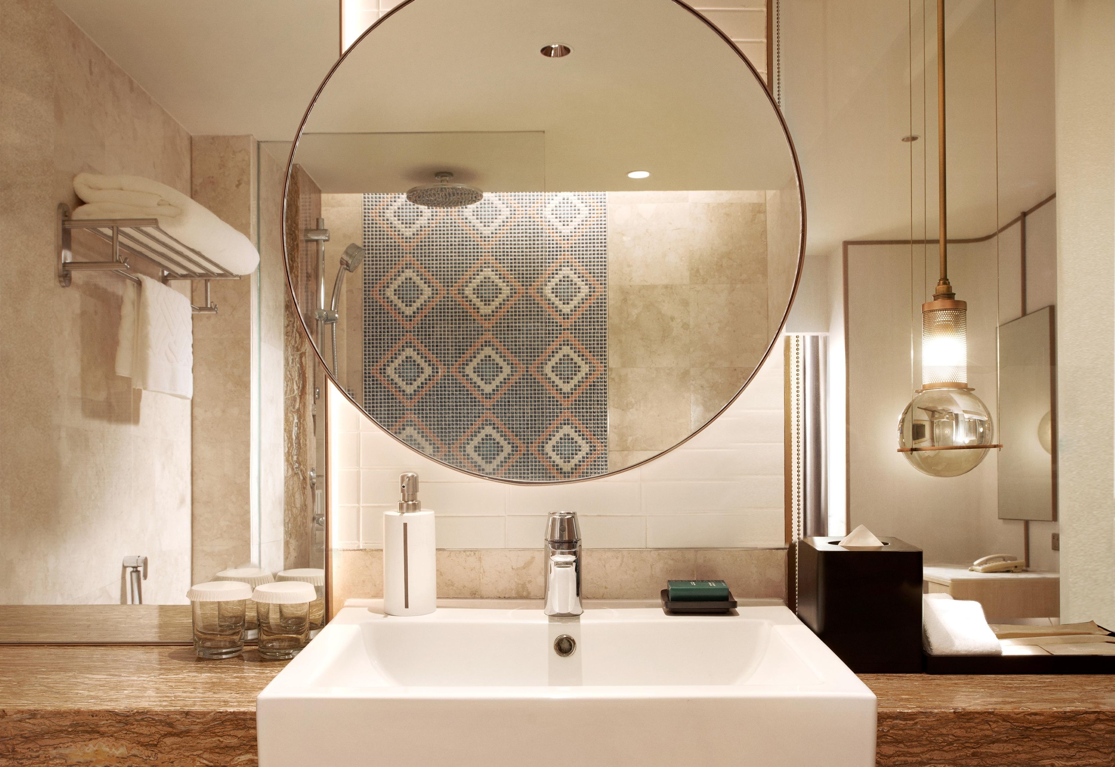 A modern bathroom with a large mirror, a rectangular sink, and a patterned shower wall.