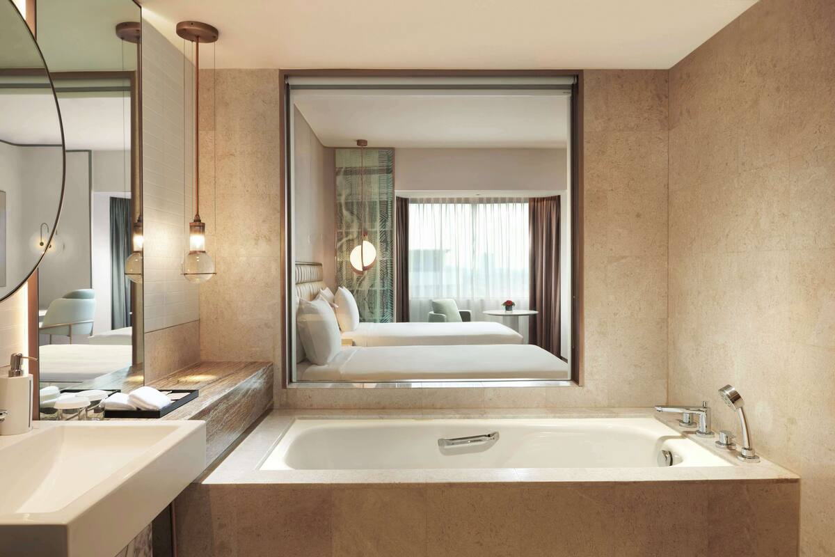 A modern bathroom with a large bathtub, a mirror, and a view into a bedroom.