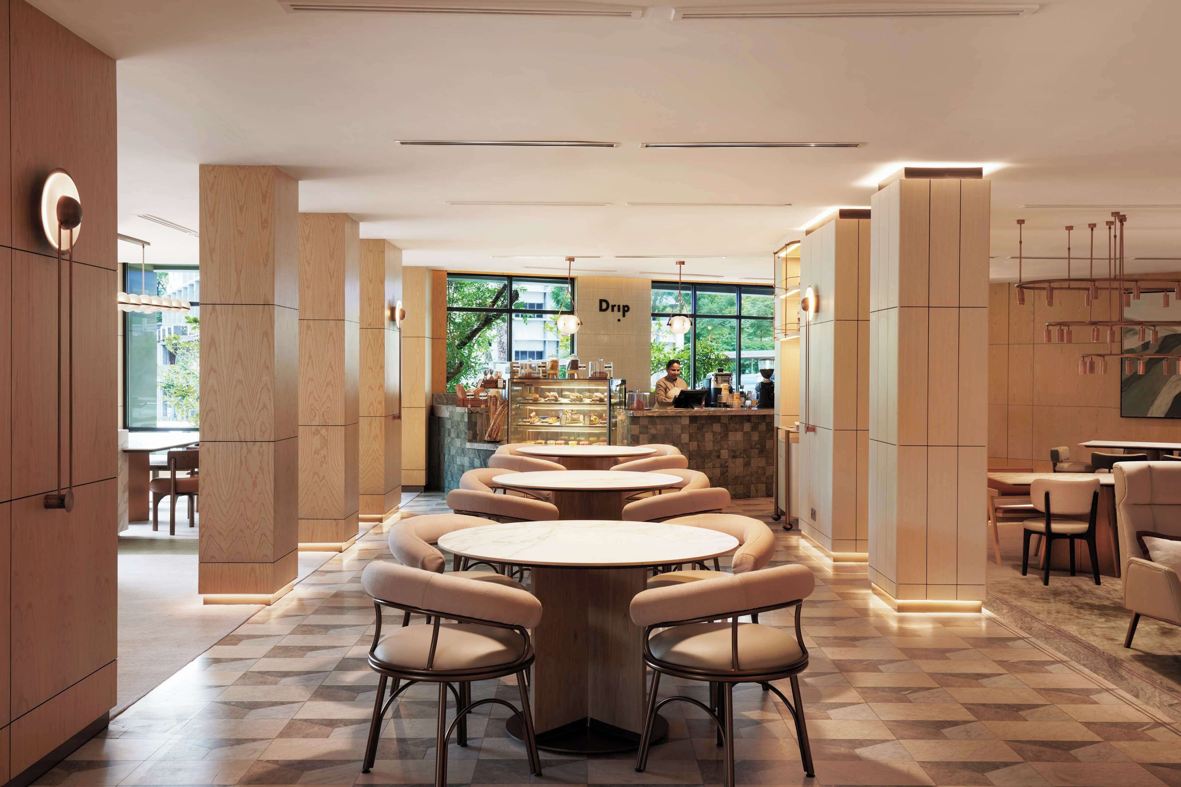 Un café moderne avec des tables et des chaises rondes, un coin bar et de grandes fenêtres donnant sur l’extérieur.