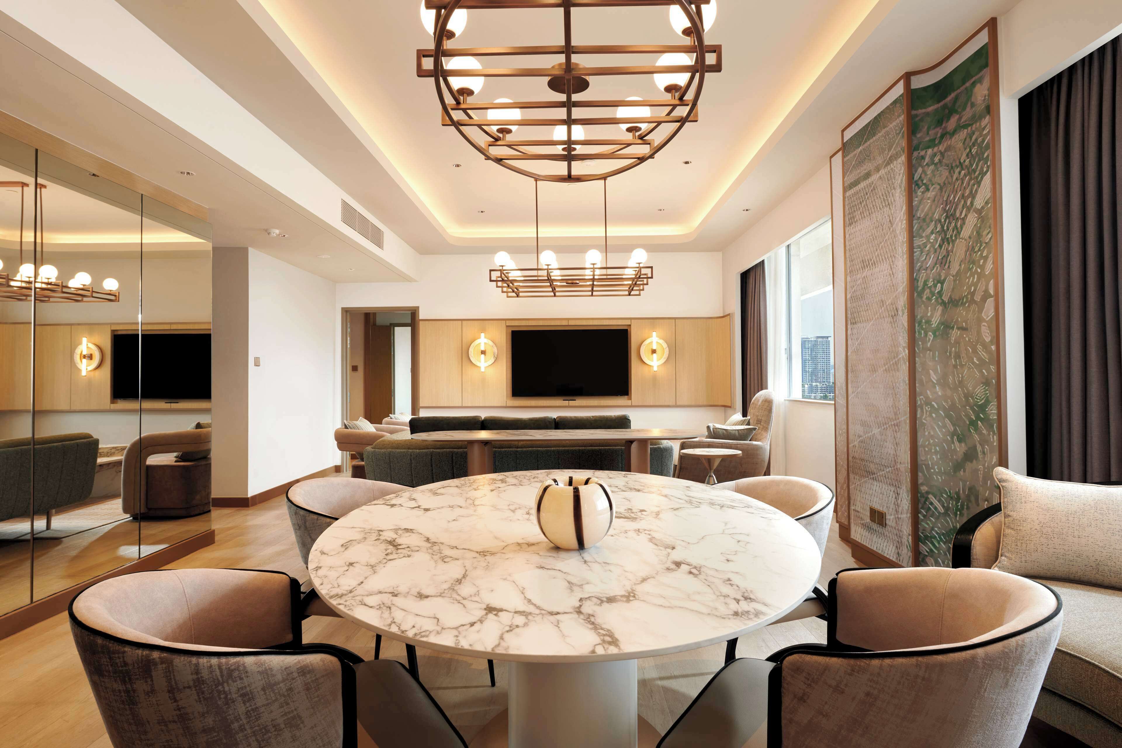 A modern living room with a marble table, comfortable seating, a large TV, and a decorative screen.