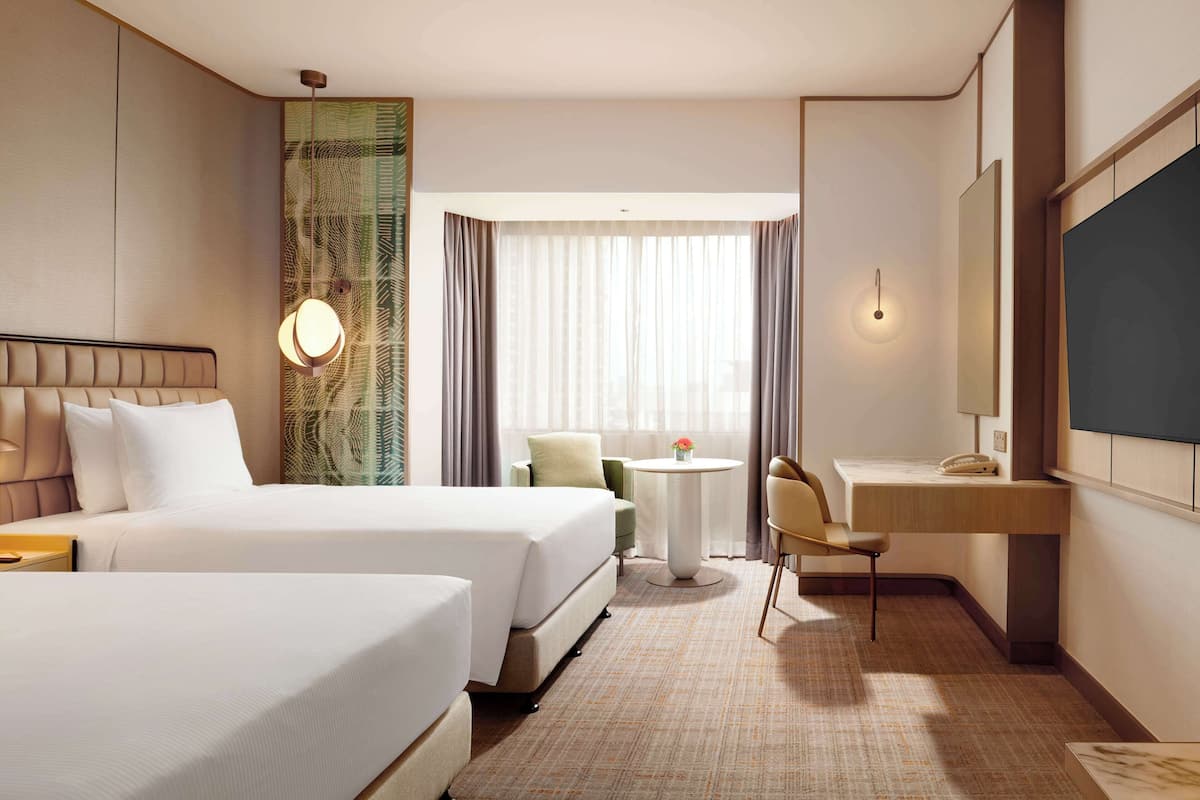 A hotel room with two beds, a desk, a chair, a small table, and a large mirror.