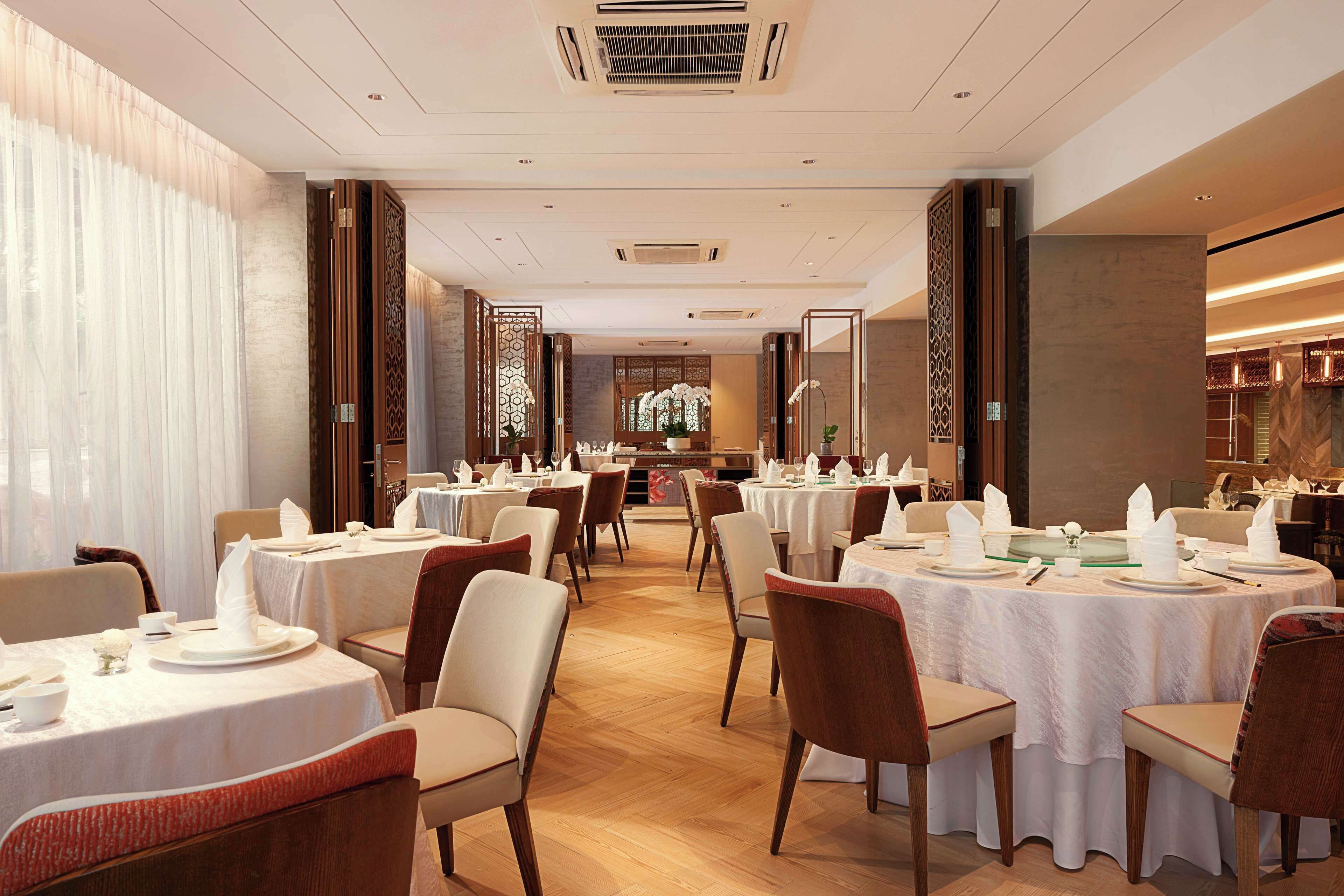 A spacious dining area with round tables set for service, featuring a modern interior design with wooden accents and a neutral color palette.