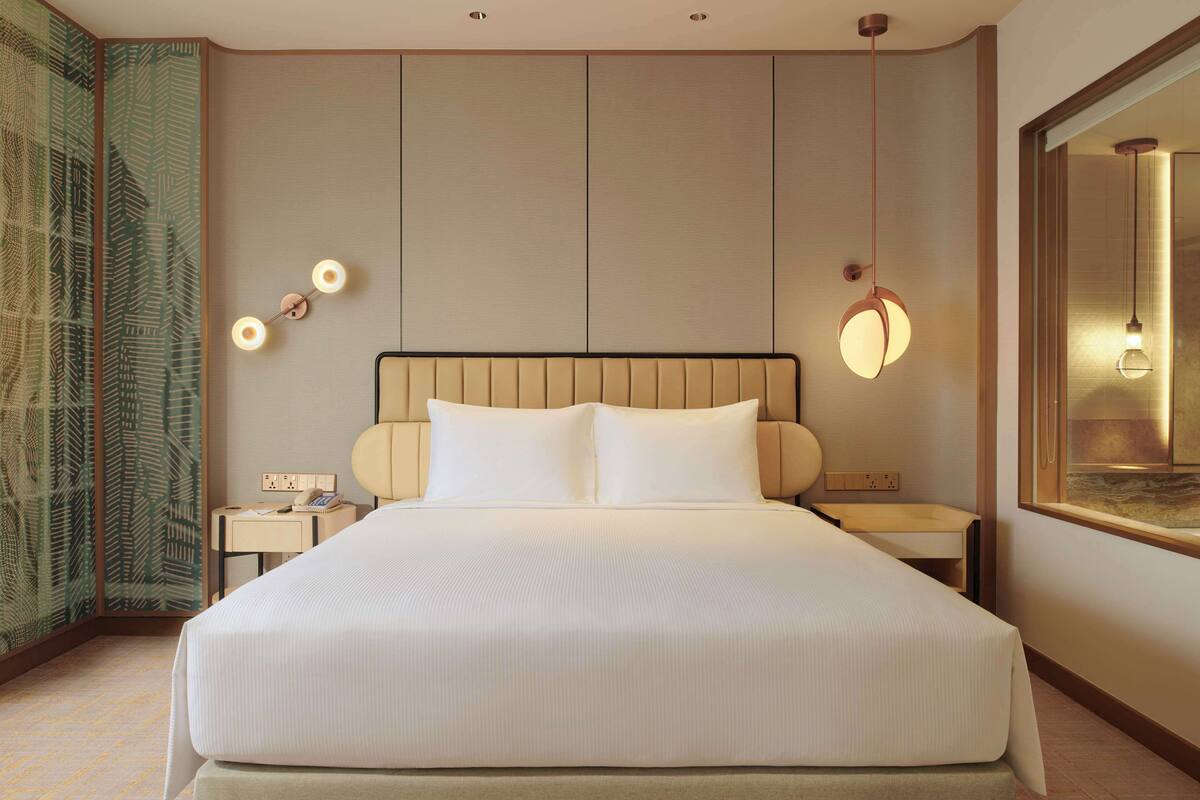 A hotel room with a large bed, bedside tables, a mirror, and a wall with a patterned wallpaper.