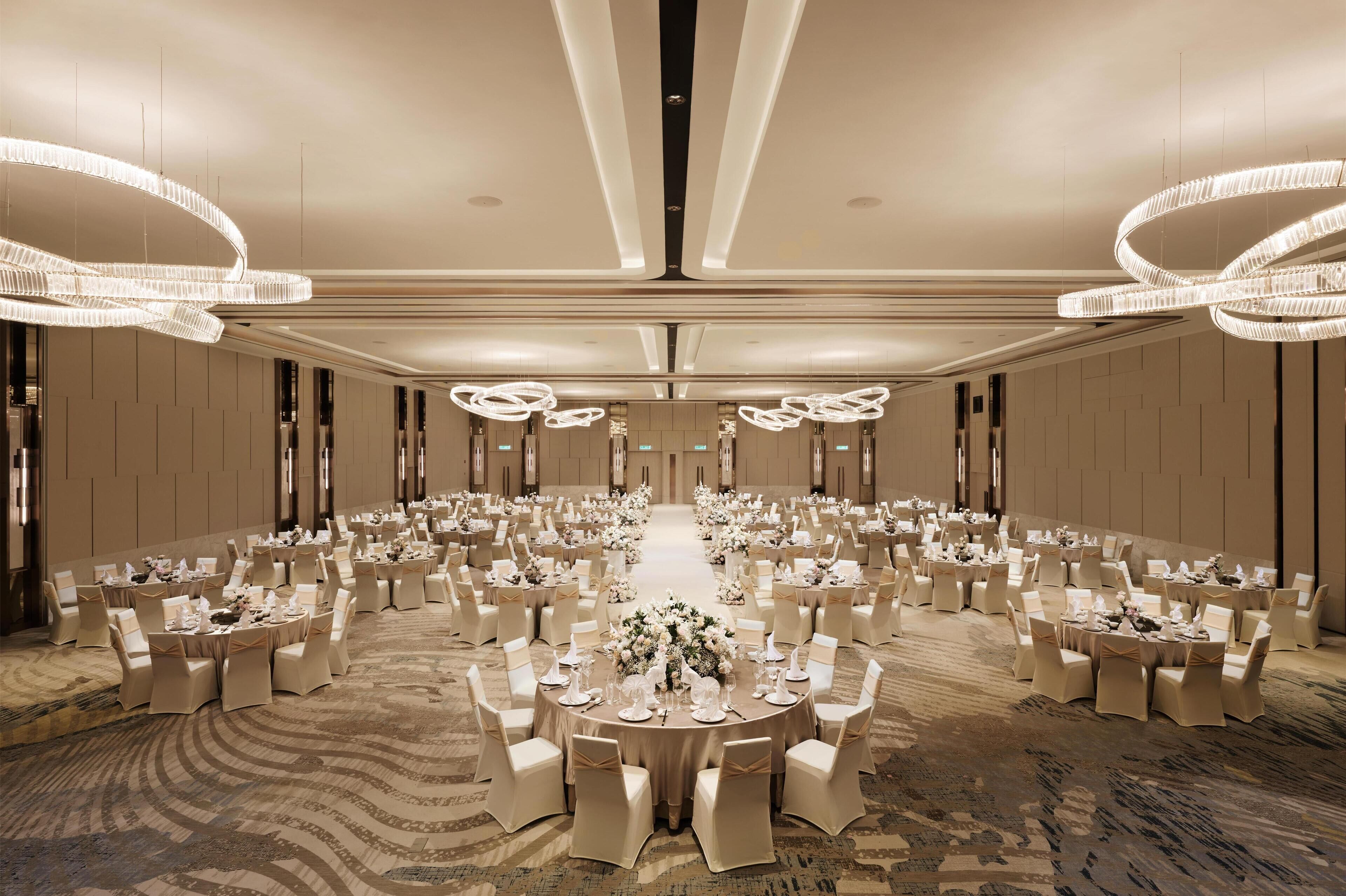 A banquet hall with round tables and chairs, chandeliers, and a carpeted floor.