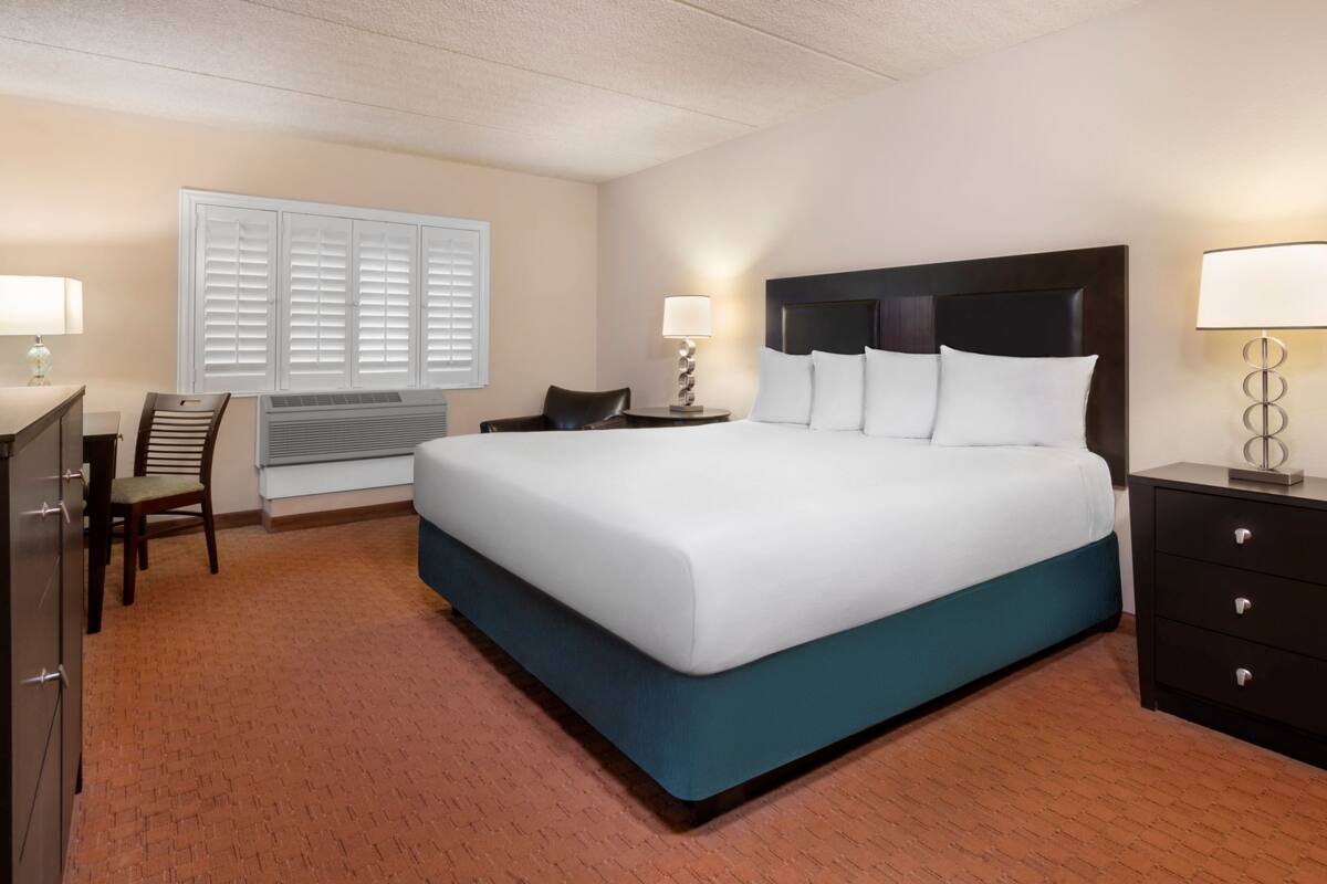 Une chambre d’hôtel avec un grand lit, un bureau, une chaise, une table de chevet et une lampe.