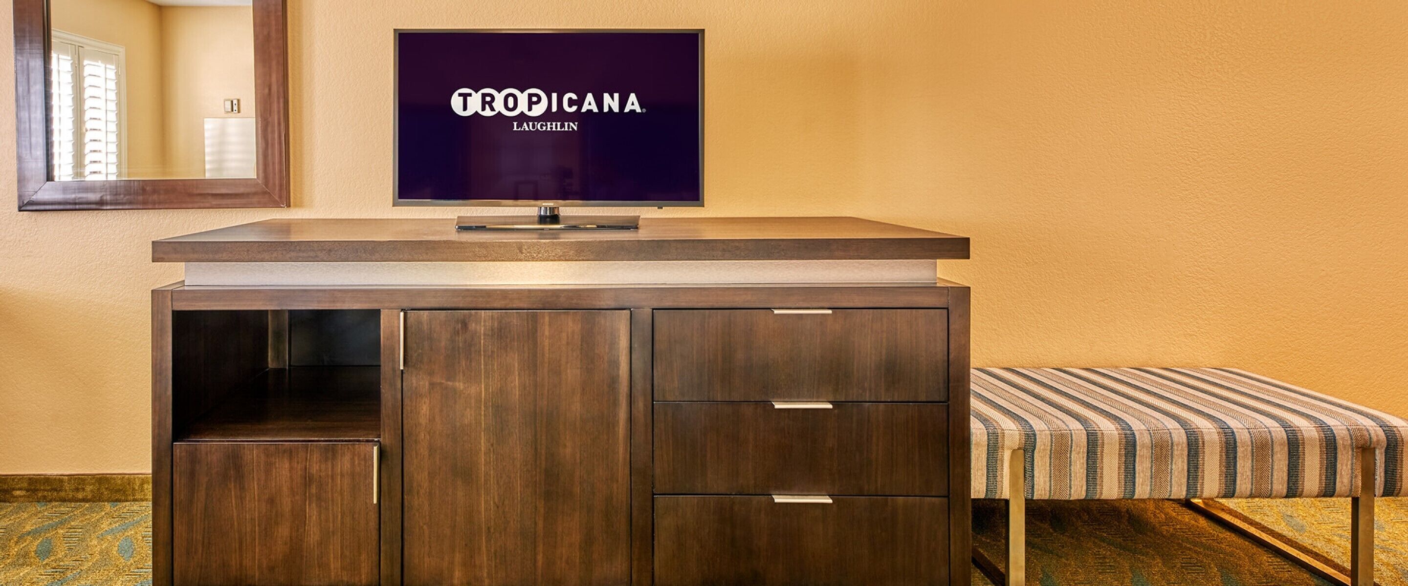 A dark wood vanity with a flat-screen TV above it displaying 'TROPICANA LAUGHLIN'.