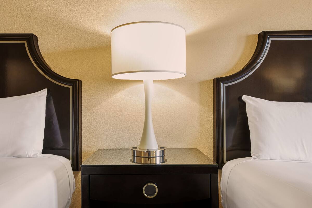 Une chambre d’hôtel avec deux lits, une table de chevet avec une lampe et un tiroir.