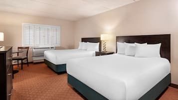 A hotel room with two beds, a desk, a chair, and a window with blinds.