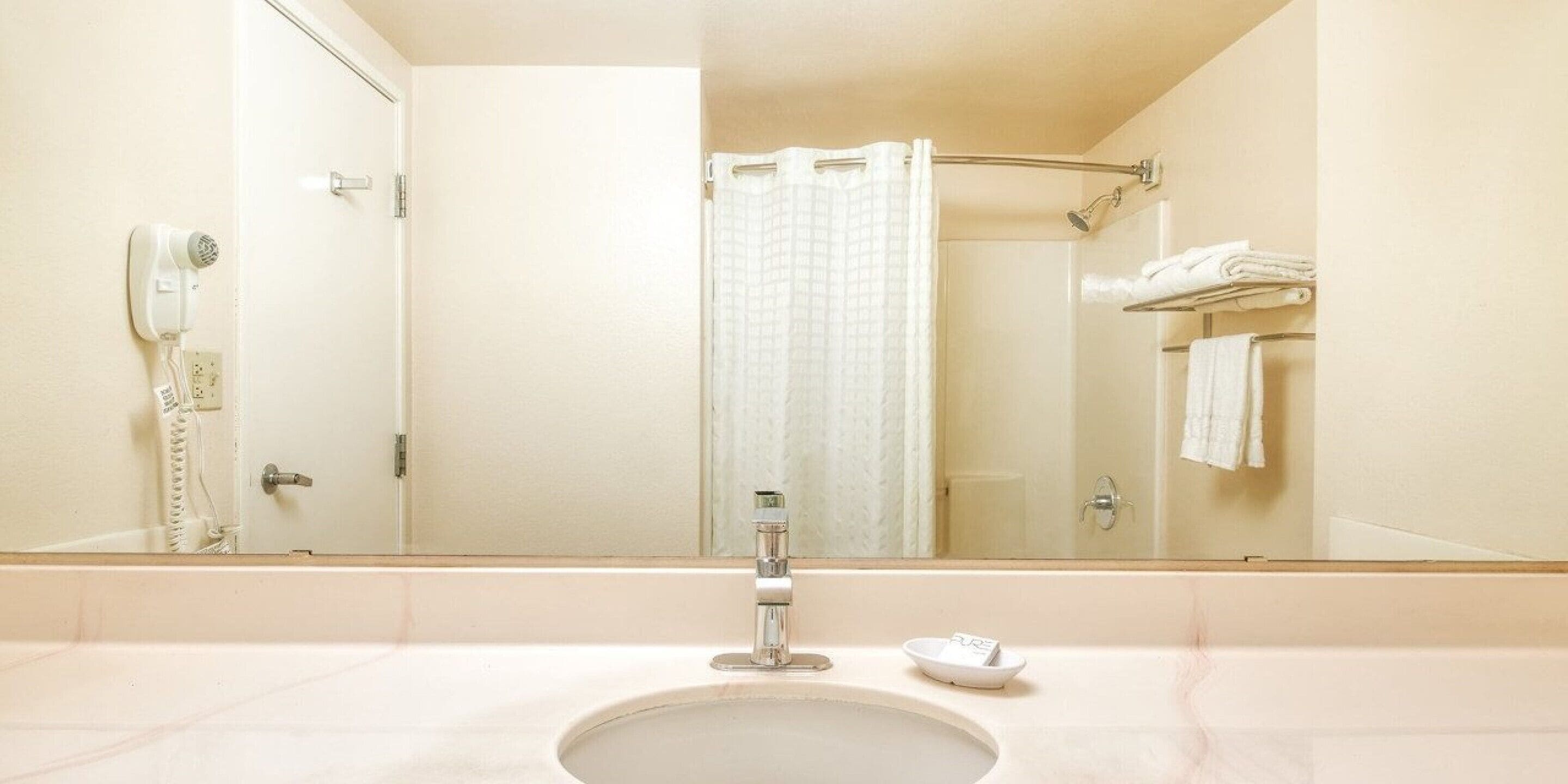 Un baño con lavamanos, espejo, cortina de ducha y toallero con toallas dobladas.