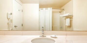 Un baño con lavamanos, espejo, cortina de ducha y toallero con toallas dobladas.