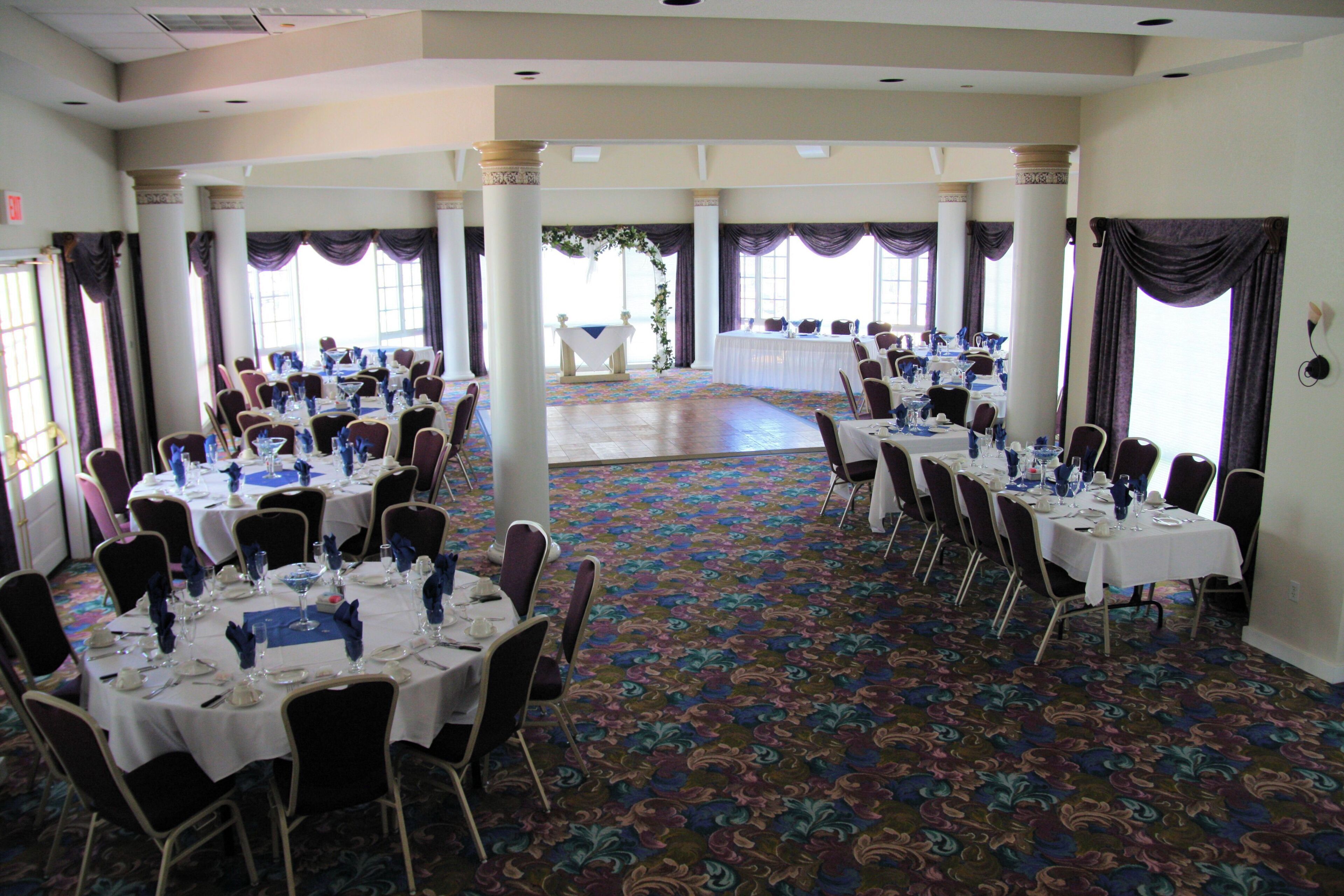 A banquet hall with multiple round tables, chairs, and a carpeted floor.