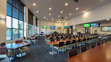 Un salón de conferencias con varias mesas y sillas, amplias ventanas y pantallas digitales mostrando información.