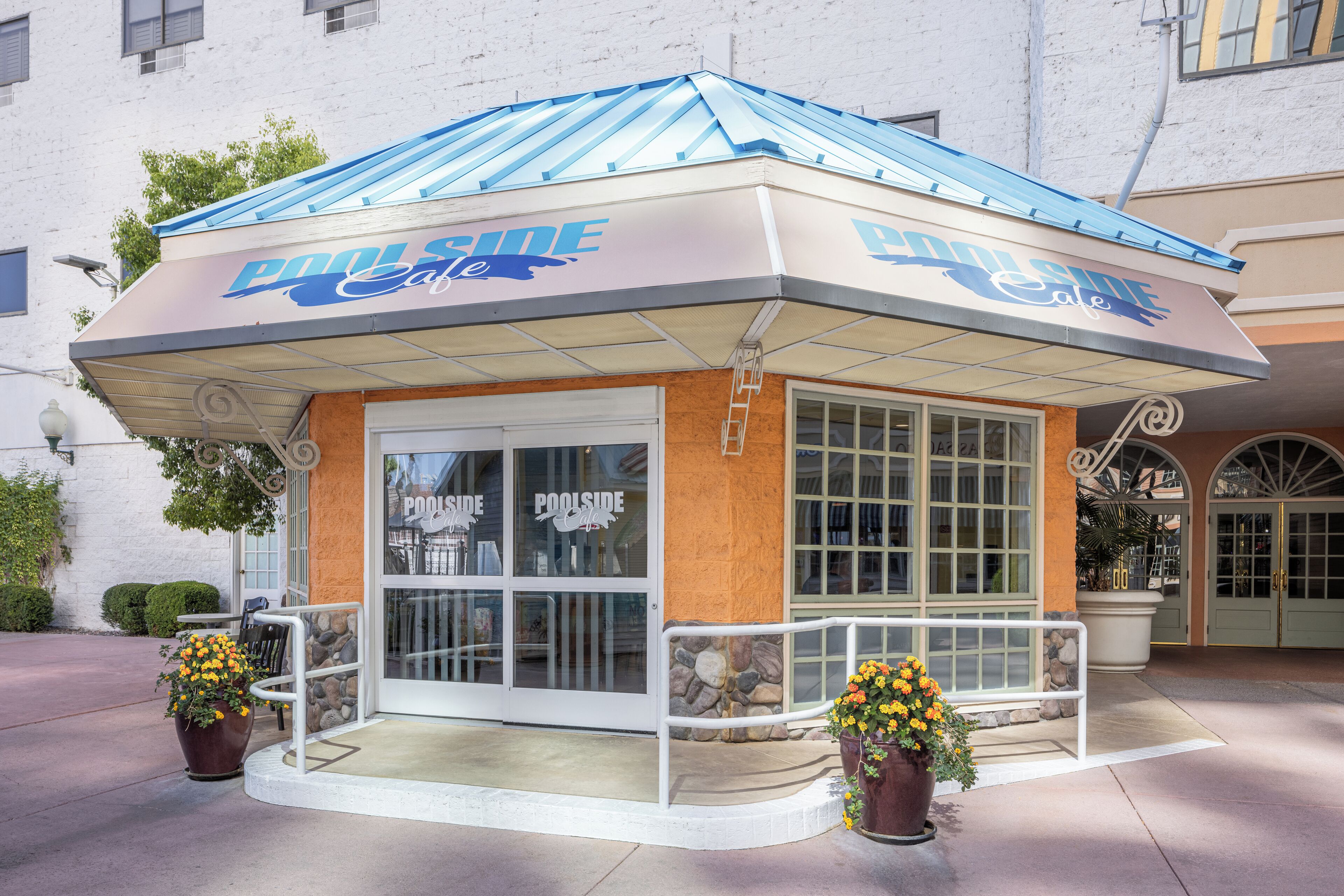 Ein Poolside-Café mit blauem Dach und weißer Fassade, mit großen Fenstern und einer Wand aus Stein.