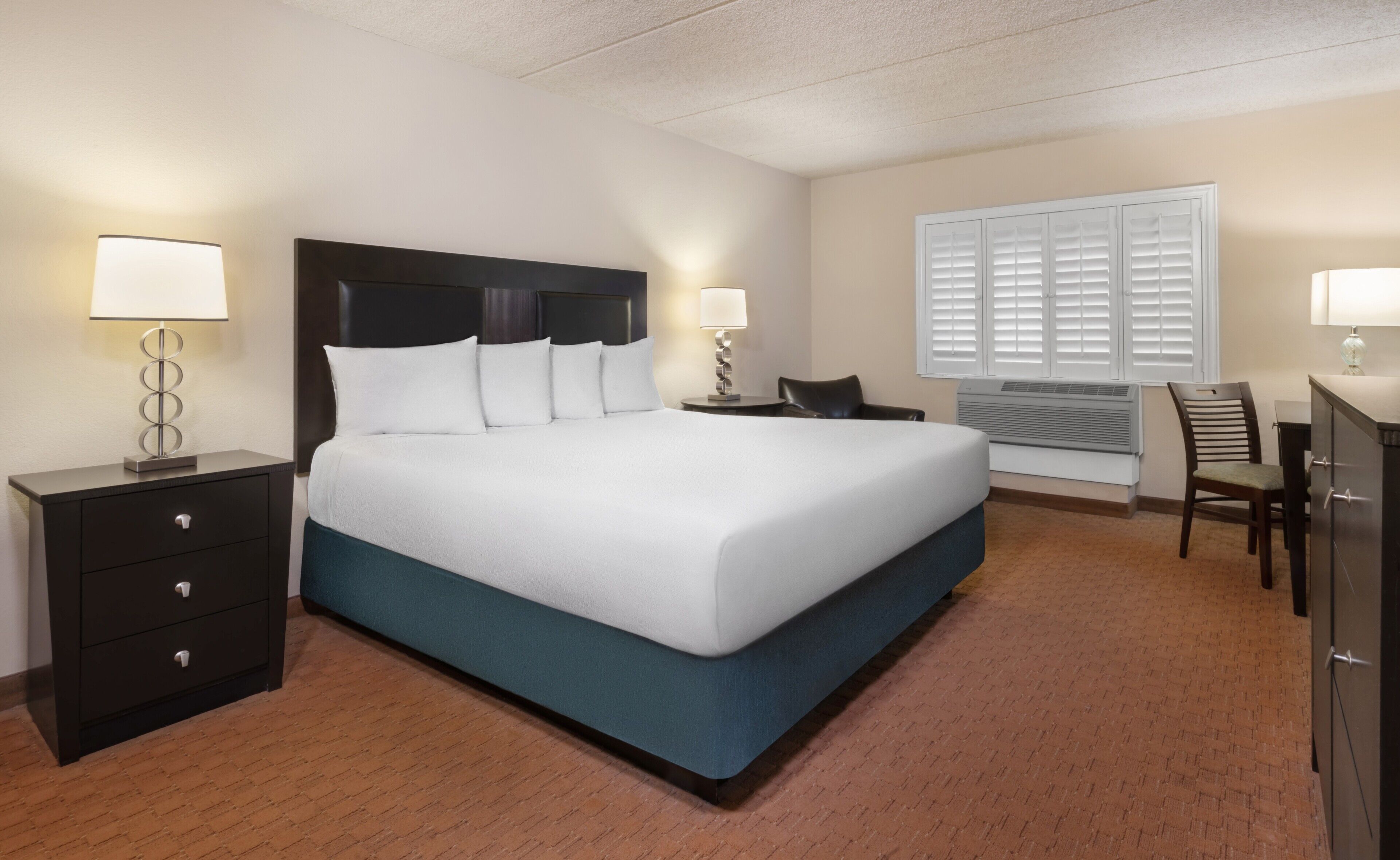 A hotel room with a large bed, two bedside tables with lamps, a desk, and a chair.