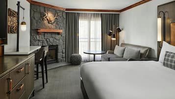 A hotel room with a large bed, a desk with a chair, a fireplace, a sofa, and a small round table.
