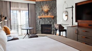 A modern hotel room with a large bed, a fireplace, a television, and a stone accent wall.