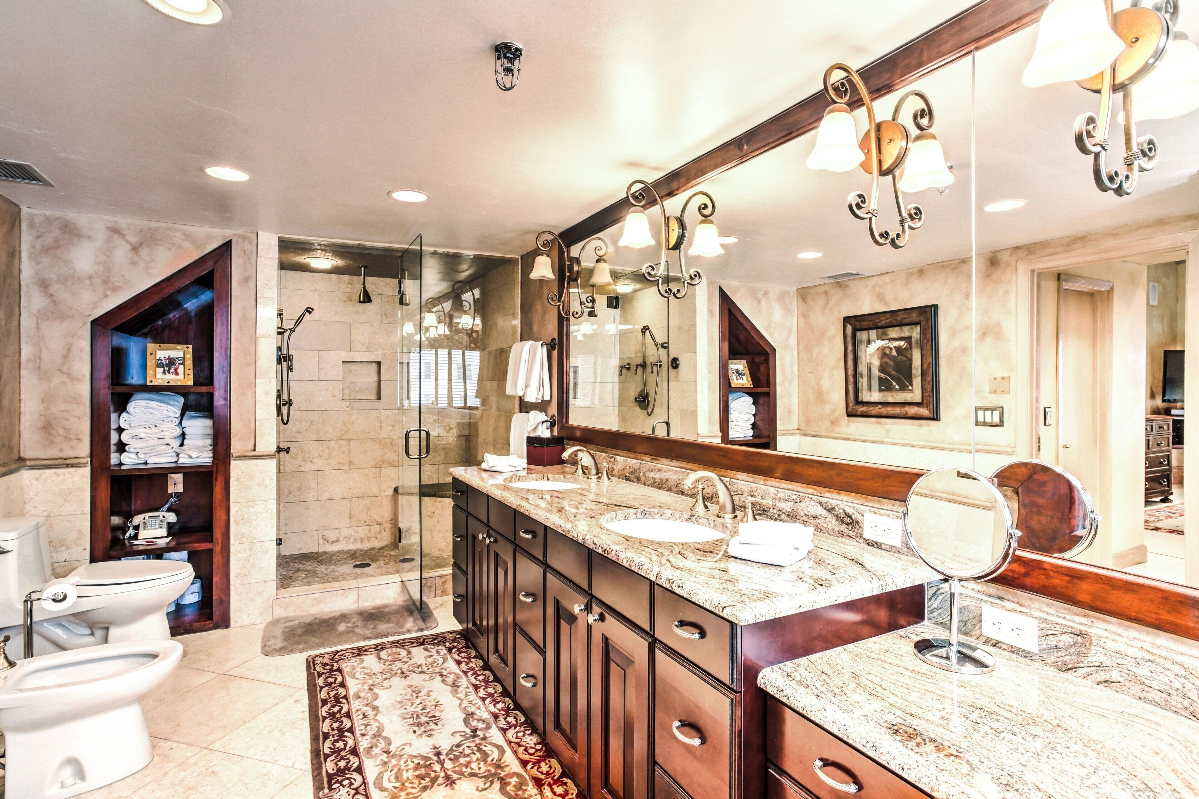 A spacious bathroom with a large vanity, double sinks, a walk-in shower, and a marble floor.