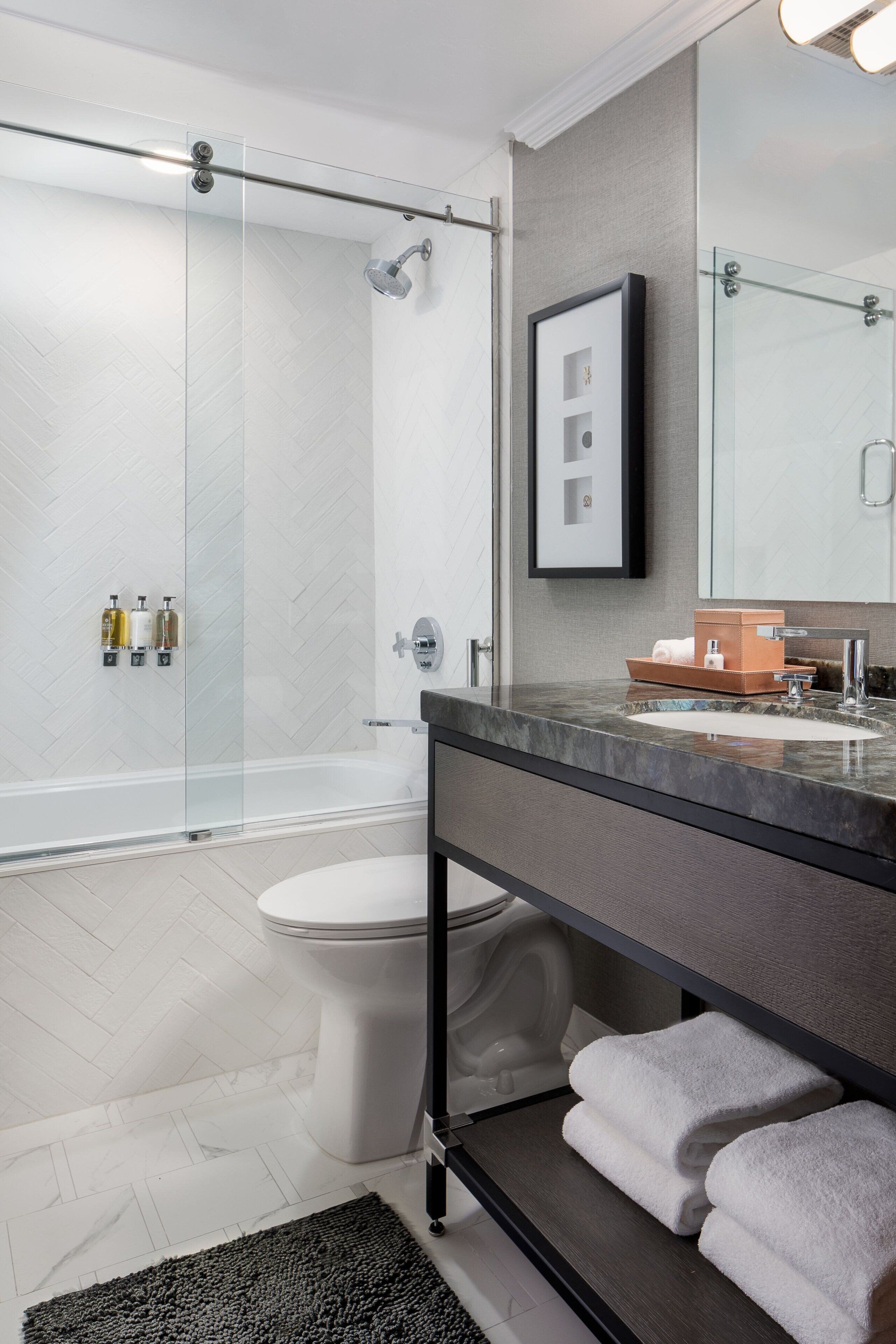 Un baño moderno con cabina de ducha de vidrio, inodoro blanco, tocador con espejo y toallero.