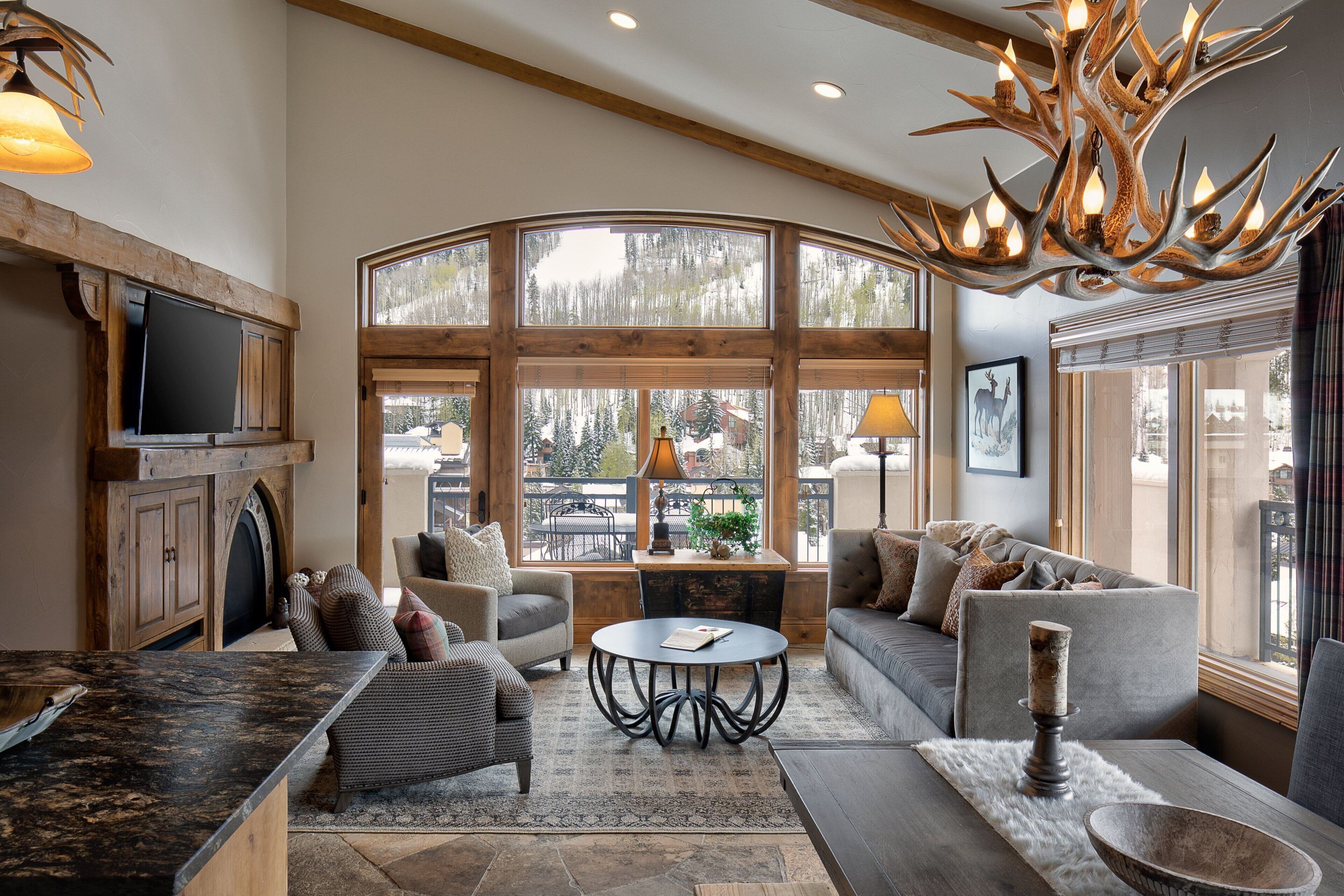 A spacious living area with a fireplace, large windows, and a modern chandelier.