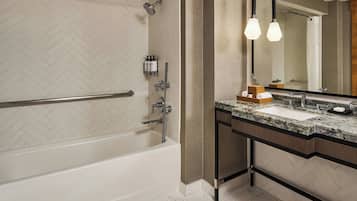 A modern bathroom with a herringbone tile backsplash, a freestanding bathtub, a vanity with a marble countertop, and a large mirror.