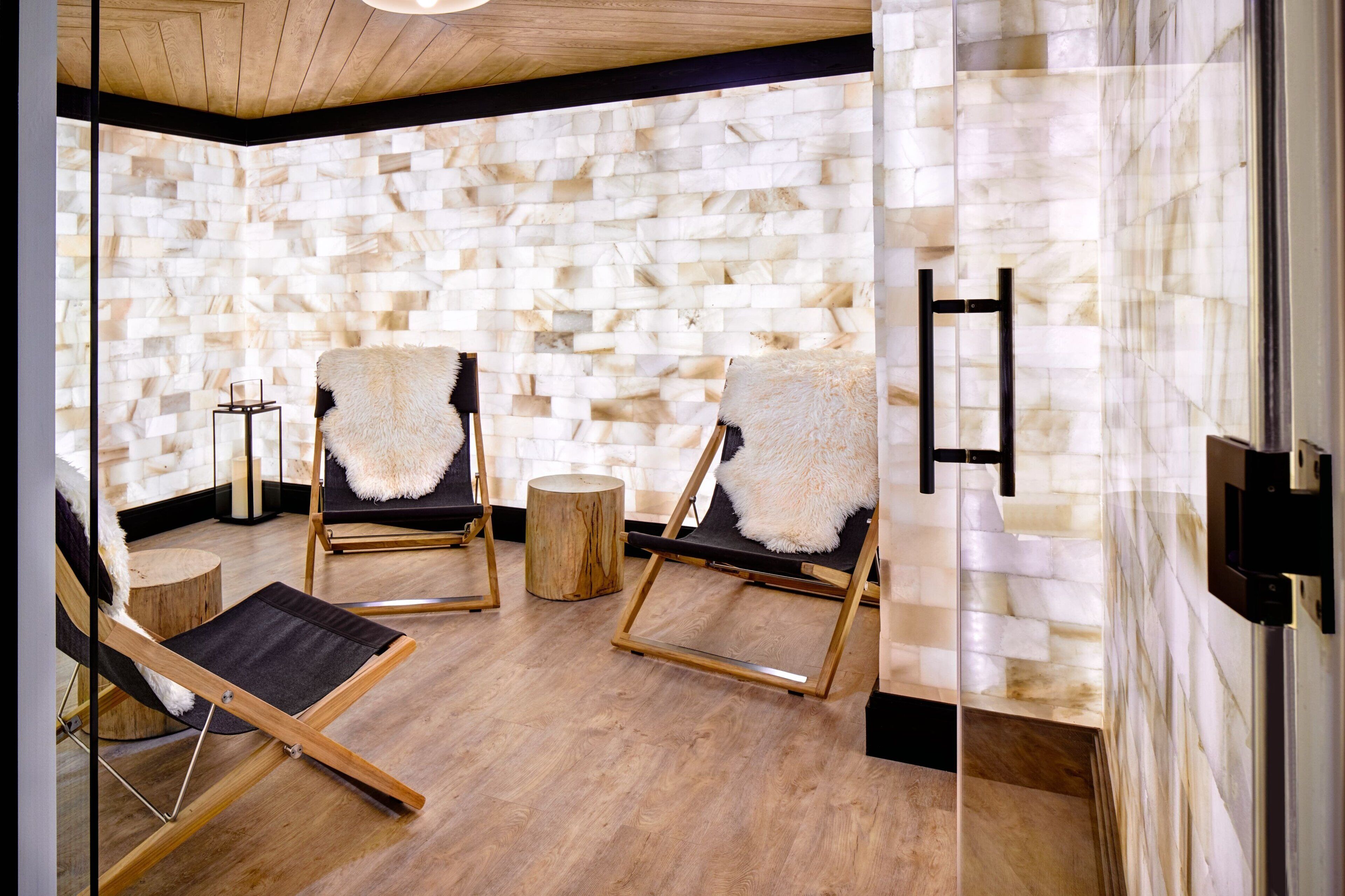 A spa room with two wooden chairs, a wooden stool, and a glass partition.