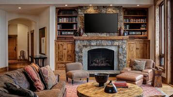 A cozy living room with a stone fireplace, leather sofas, a coffee table, and bookshelves filled with books.