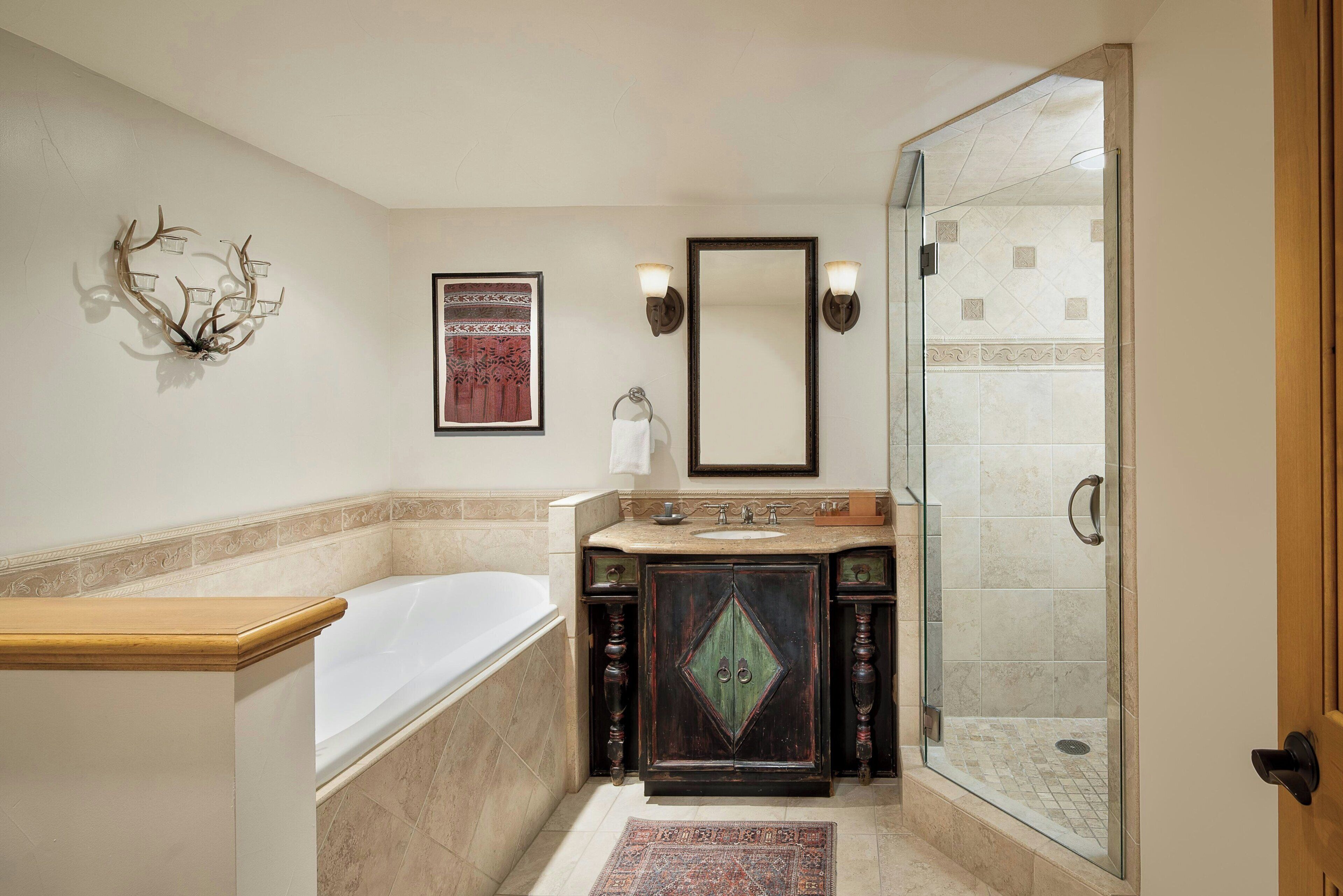 A bathroom with a bathtub, a glass-enclosed shower, a vanity with a mirror, and a wall-mounted light fixture.
