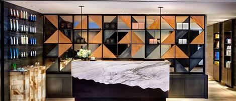 A modern hotel lobby with a marble reception desk, geometric wall panels, and a display of toiletries.