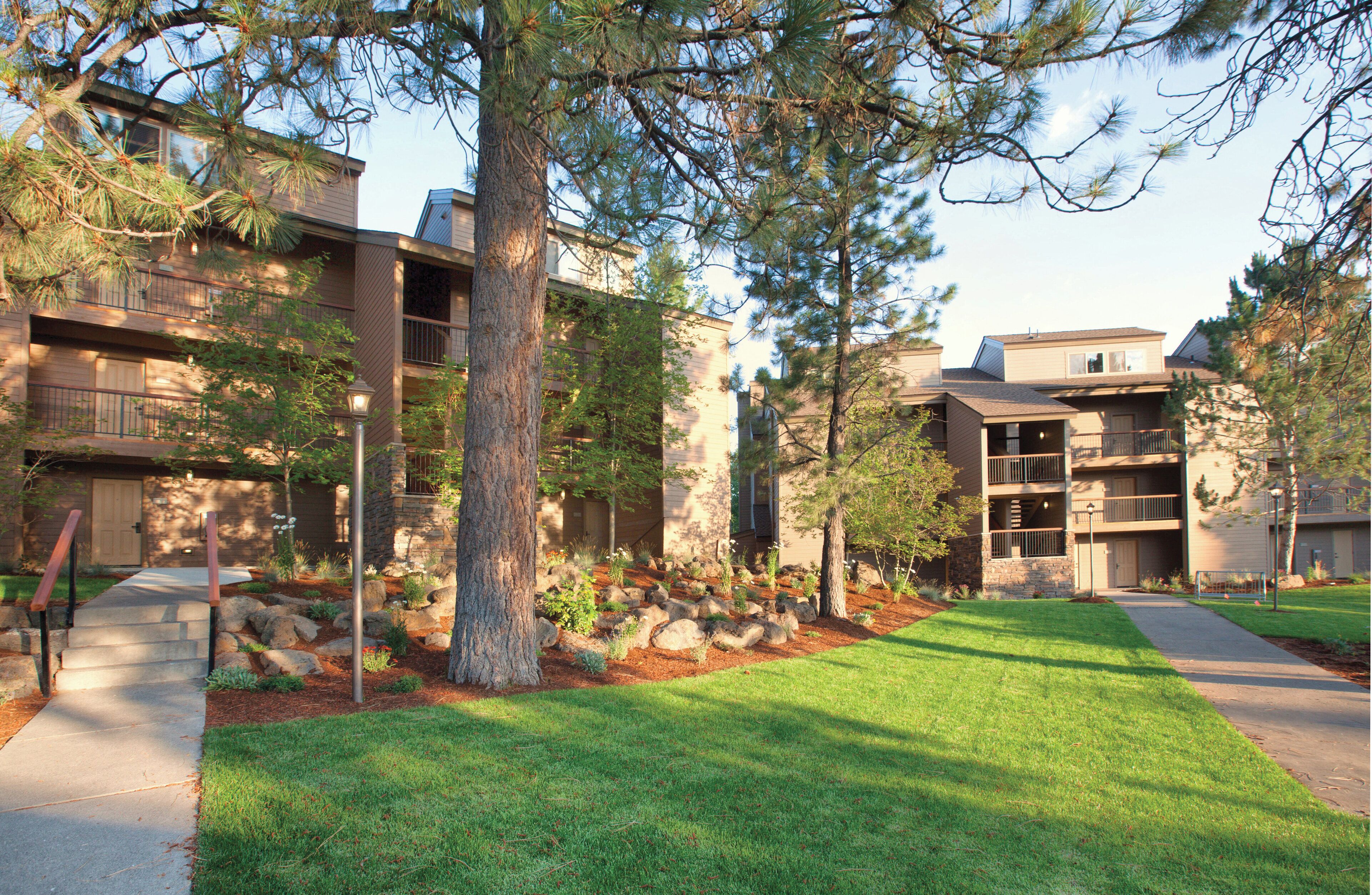 A residential building with multiple balconies, a well-maintained lawn, and a stone pathway leading to the entrance.