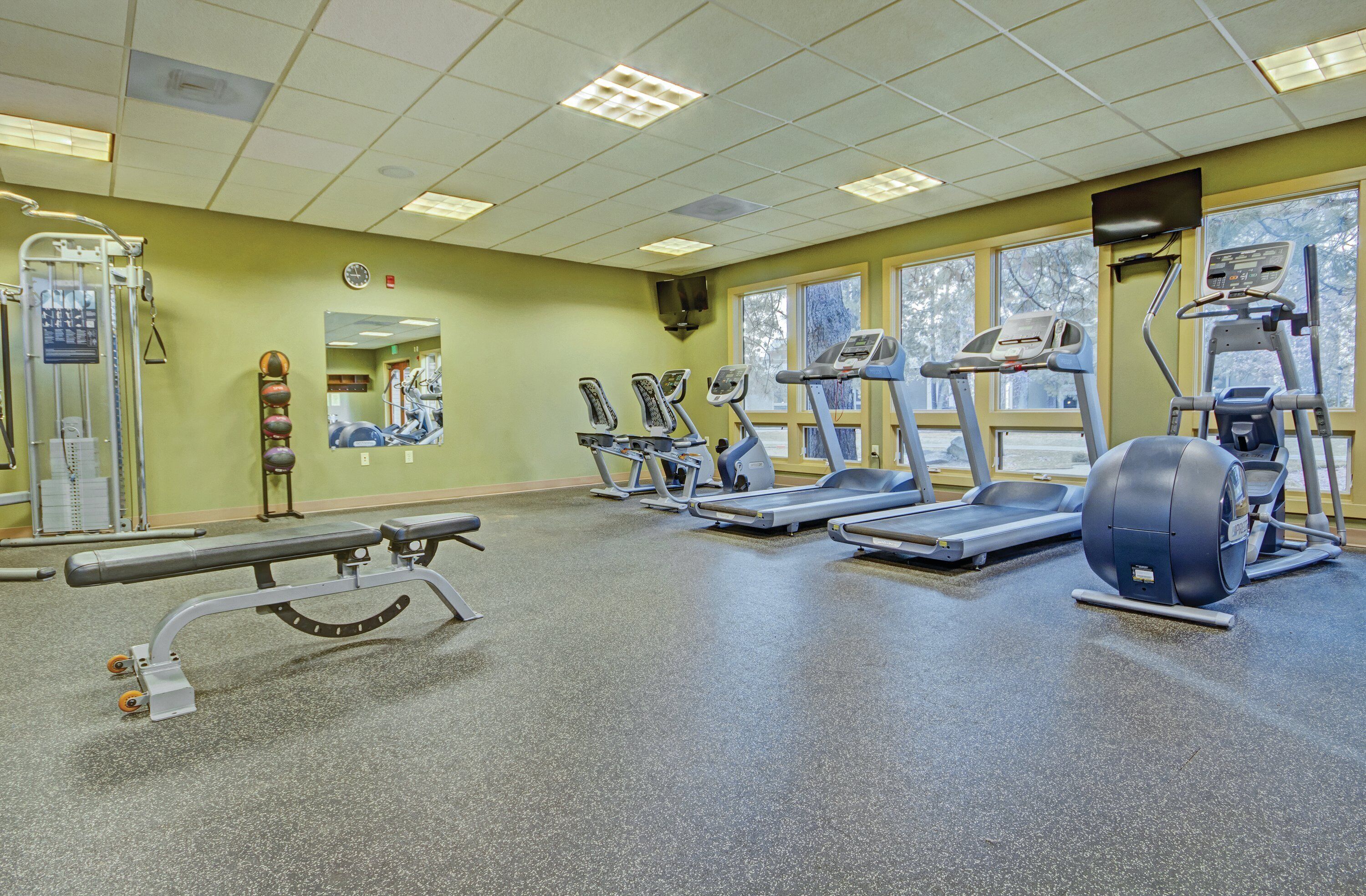Een fitnessruimte met loopbanden, elliptische trainers en een halterbank.