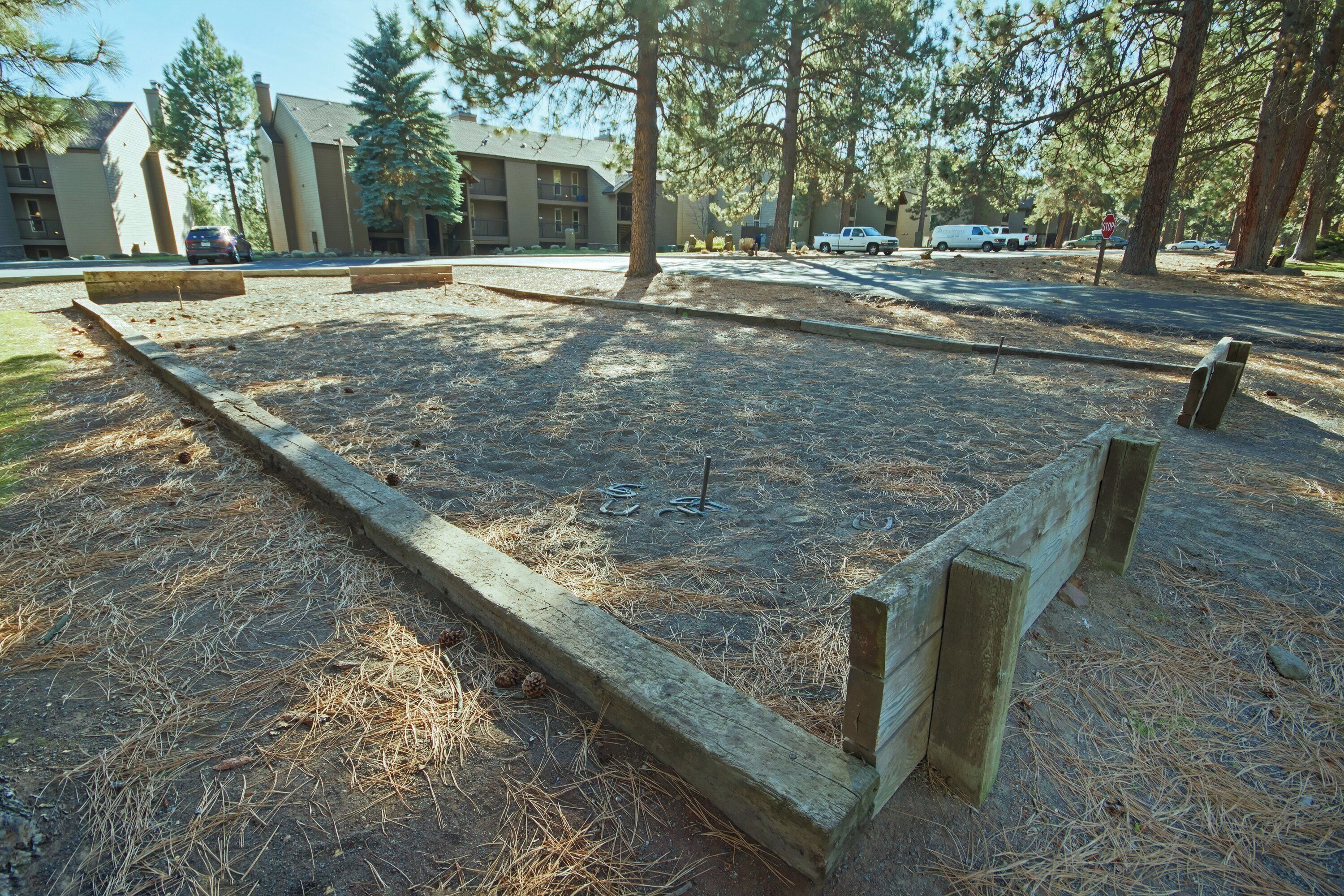 Una terraza de madera cuadrada con estacas metálicas en el centro, rodeada de agujas de pino secas y hierba.