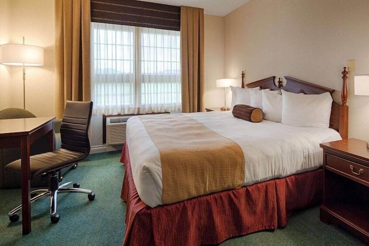 A hotel room with a large bed, two bedside lamps, a desk with a chair, and a window with curtains.